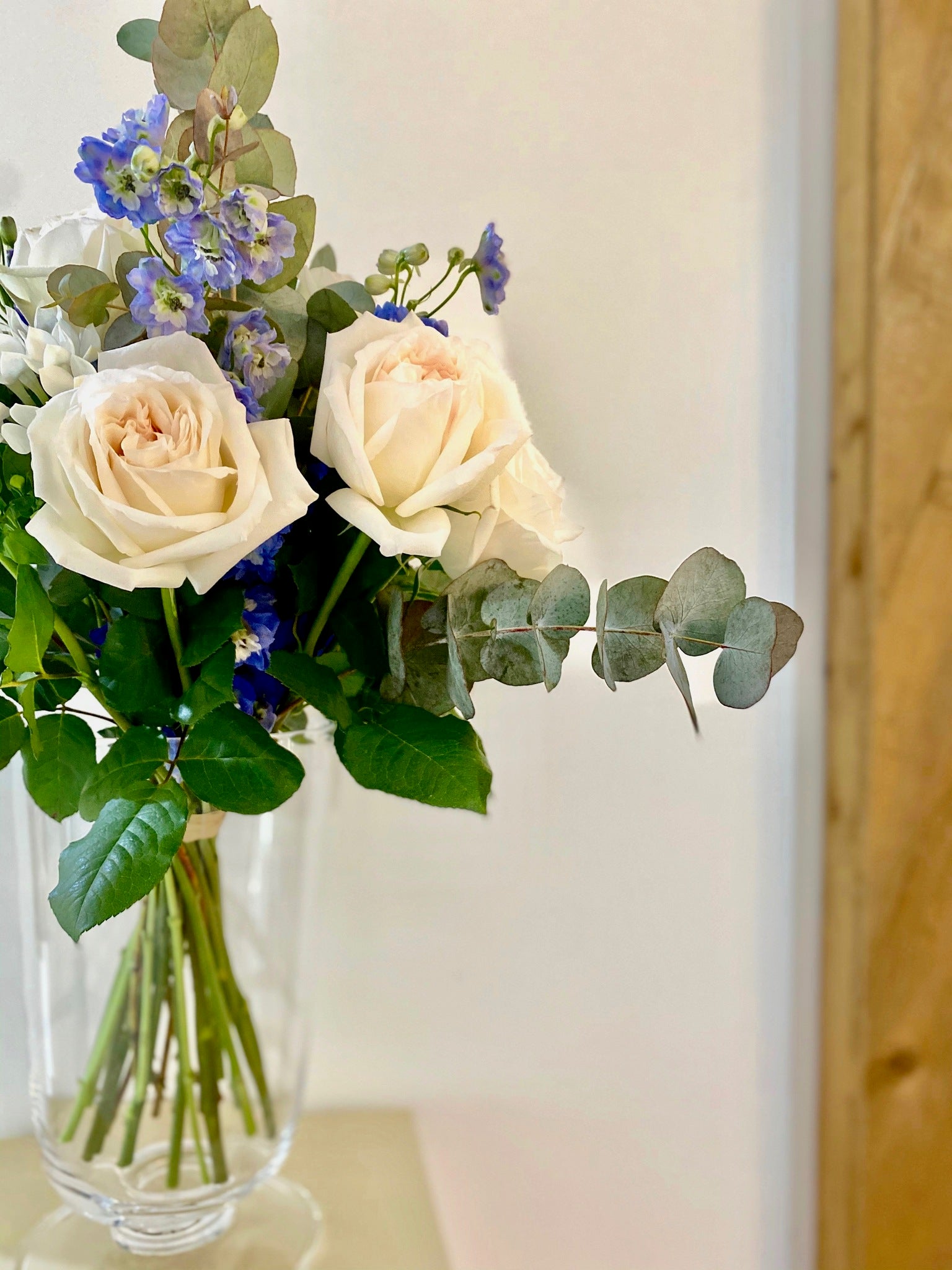 Aimee bouquet by Margot Floral Design. A fresh flower bouquet composed of White O'Hara Garden Roses, Blue Delphiniums, White Bouvardias, and Eucalyptus. Small size.