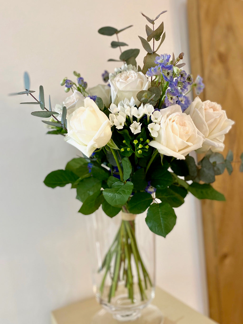 Aimee bouquet by Margot Floral Design. A fresh flower bouquet composed of White O'Hara Garden Roses, Blue Delphiniums, White Bouvardias, and Eucalyptus. Small size.