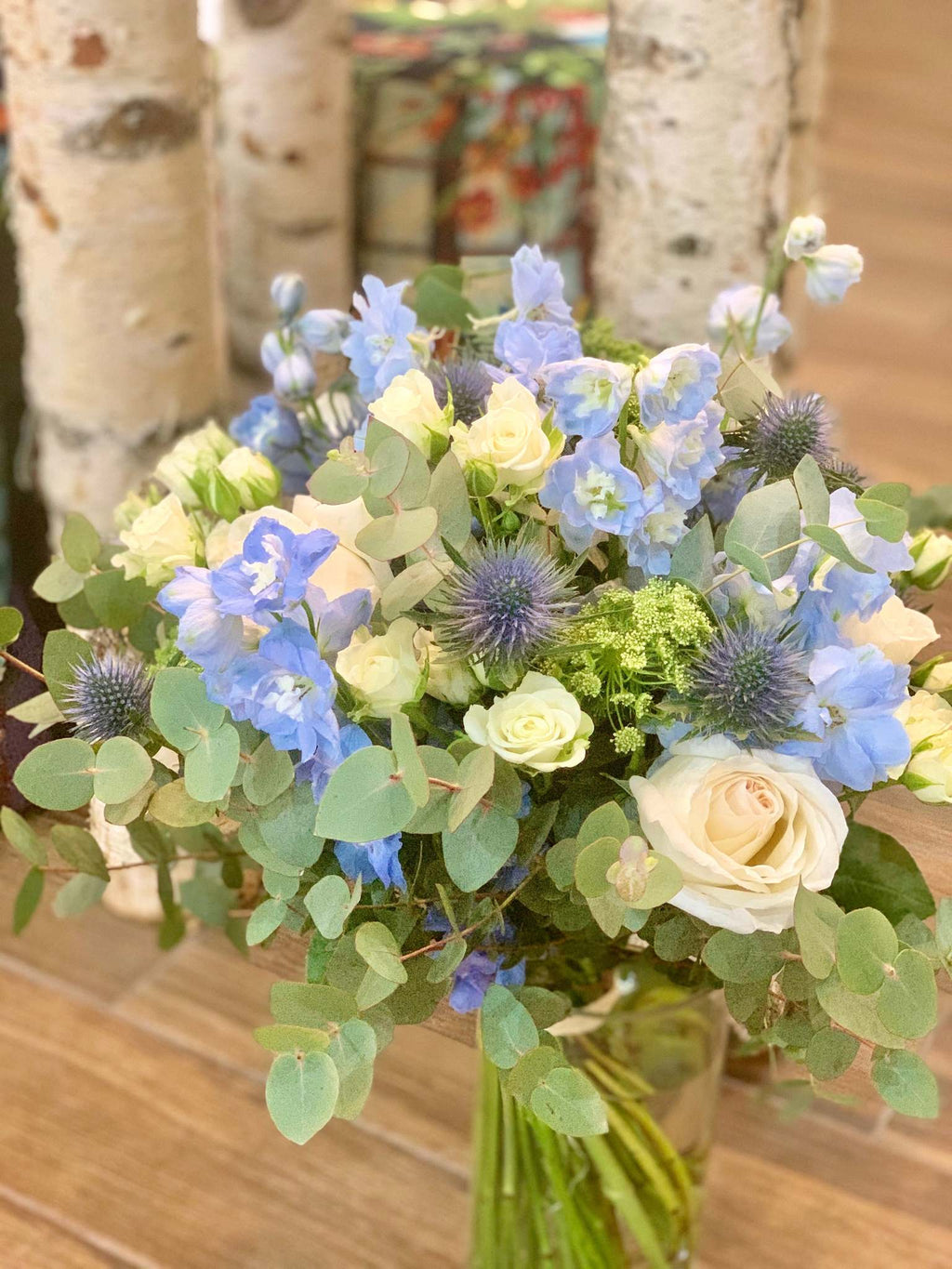 Josephine bouquet by Margot Floral Design. A fresh flower bouquet composed of White O'Hara Garden Roses, Blue Delphinium, Eryngium, and Eucalyptus. Medium size.