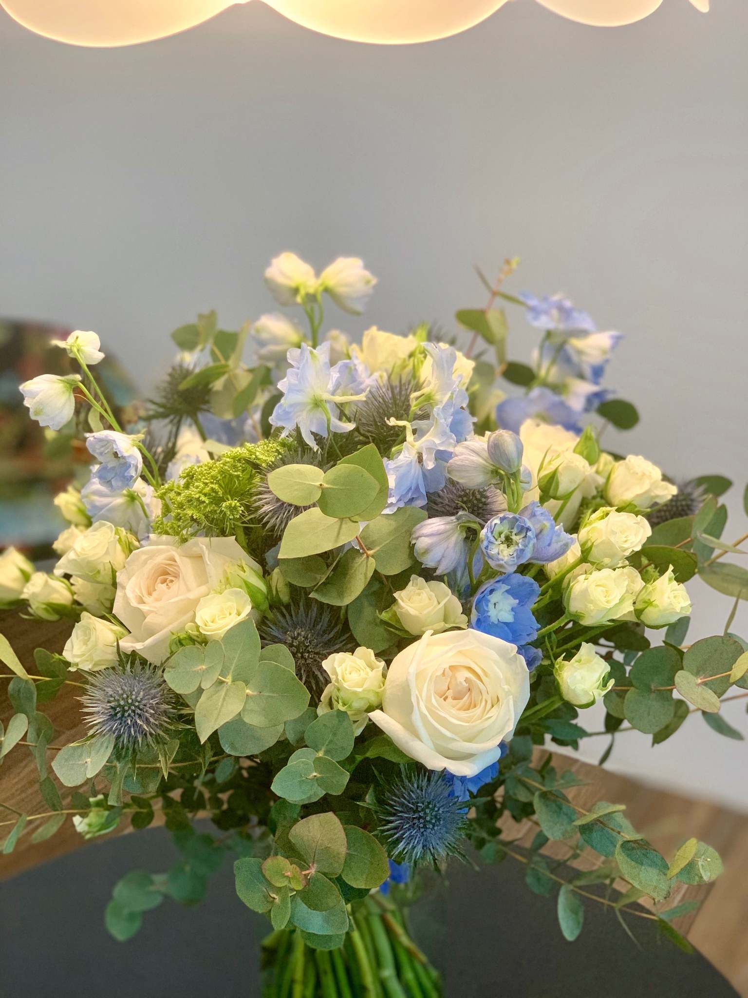 Josephine bouquet by Margot Floral Design. A fresh flower bouquet composed of White O'Hara Garden Roses, Blue Delphinium, Eryngium, and Eucalyptus. Medium size.