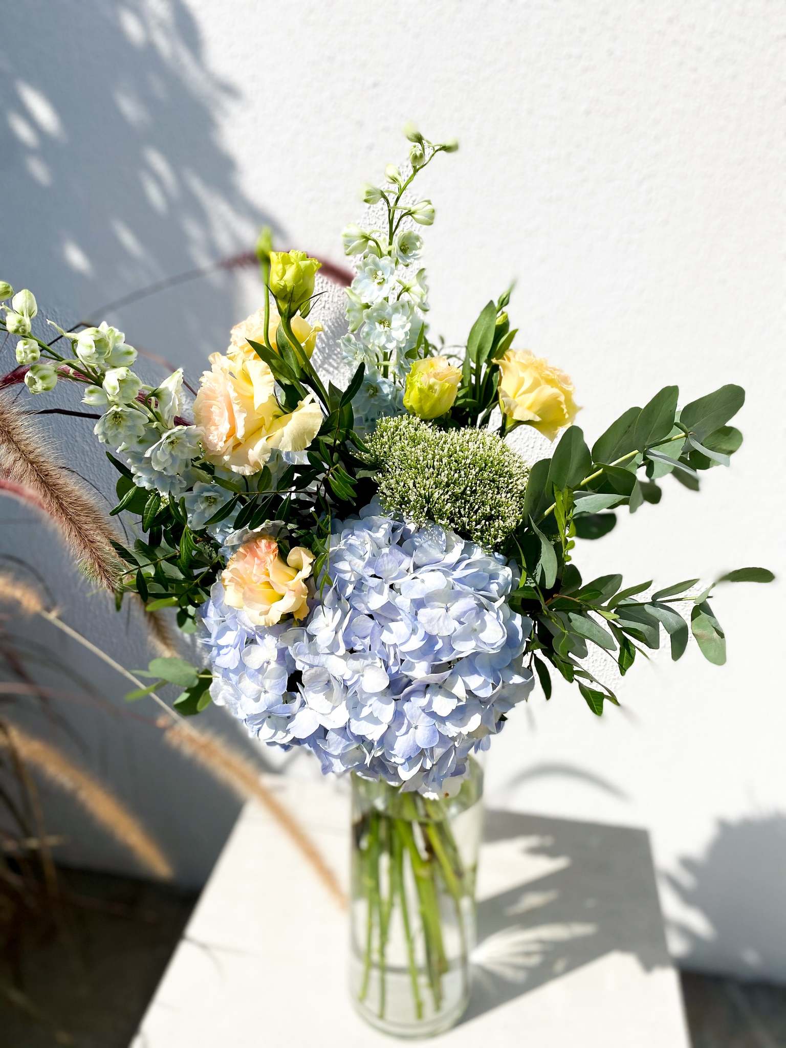 Valentine bouquet by Margot Floral Design. A fresh flower bouquet composed of Pale Yellow Roses, White Delphinium, Blue Hydrangea, and Eucalyptus. Small Size.