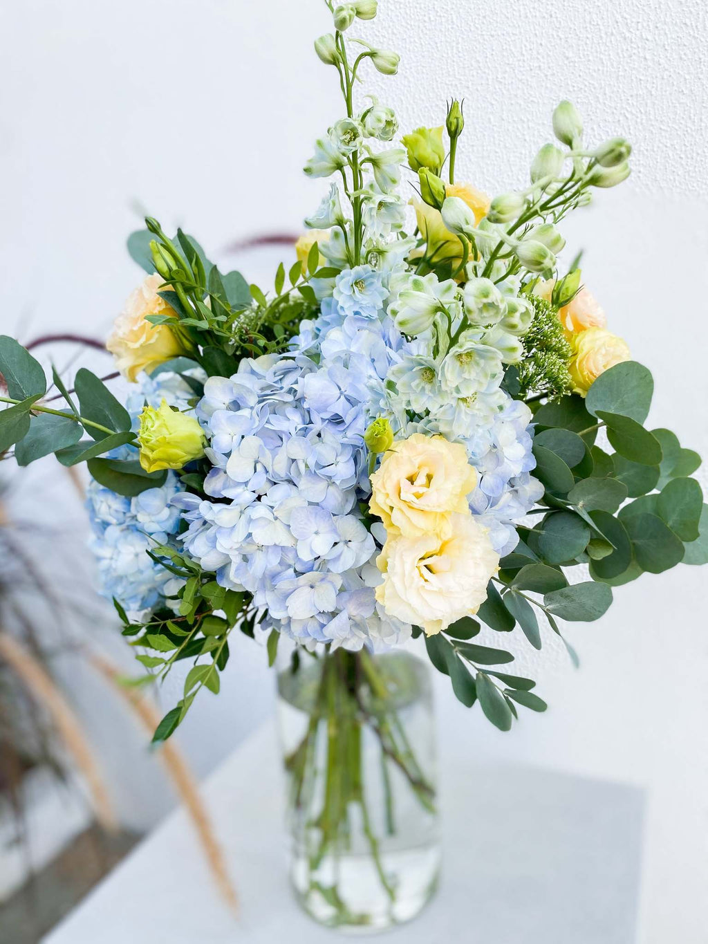 Valentine bouquet by Margot Floral Design. A fresh flower bouquet composed of Pale Yellow Roses, White Delphinium, Blue Hydrangea, and Eucalyptus. Large Size.